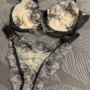Blommig svart spets bralette BH och Trosor  - Snygg bralette BH och Trosor i transparent mesh med svarta broderade blommor och tunna axelband. Toppens mesh är beige med svarta detaljer och har en feminin, romantisk vibe. Perfekt för att styla under en öppen skjorta eller kavaj.