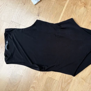 Svart ärmlös bodysuit från boohoo - Säljer en svart, stilren bodysuit från bohoo. Modellen är ärmlös med rund halsringning och har en tight passform som sitter snyggt mot kroppen. Perfekt att styla med jeans eller kjol för en clean look.