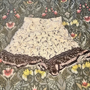 Mönstrade volang Kjol shorts från H&M - Supersöta kjolahort från H&M i ljusbeige med svart och brunt mönster. De har volangkant nertill och ett löst, flowy fit. Perfekta för sommardagar när du vill ha något bekvämt men ändå snyggt. Materialet är mjukt och lätt, och shortsen har hög midja.