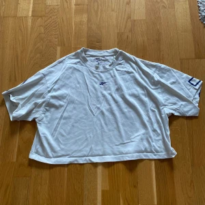 Vit croppad t-shirt från Reebok  - Säljer en vit croppad t-shirt från Reebok med blå Les Mills-tryck över ryggen och liten logga framtill. Oversized passform och korta ärmar, jättefin både på gymmet och till vardags!