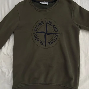 Olivgrön Stone Island sweatshirt !ÄKTA! - Olivgrön sweatshirt från Stone Island med stort broderat kompassmärke på bröstet och klassisk patch på ärmen. Tröjan har rund hals, långa ärmar och är gjord i mjuk bomull. Perfekt för dig som gillar streetwear och vill sticka ut med en ikonisk look.