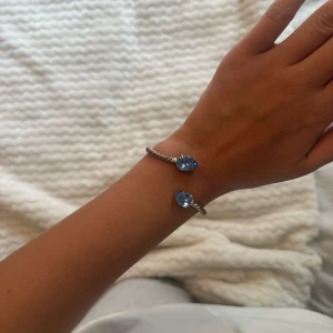 Caroline svedbom armband i silver med blå stenar - Snyggt armband i silver med tvinnad design och två stora blå droppformade stenar i varje ände. Tillverkad av caroline svedbom i italien , orginalpris 895-1000kr. I bra skick