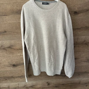 Ljusgrå randig tröja Dressmann XL - Snygg ljusgrå tröja från Dressmann i storlek XL. Tröjan har diskreta horisontella ränder och är tillverkad i ett mjukt, stickat material. Rund halsringning och långa ärmar gör den perfekt för lager-på-lager-stil.