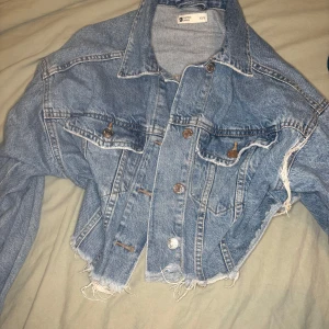 Croppad jeansjacka från Perfect Jeans - Säljer en croppad ljusblå jeansjacka från Perfect Jeans. Jackan har råa, fransiga kanter nertill, klassisk krage, bröstfickor med knappar och långa ärmar. Perfekt för dig som vill ha en chill och trendig look.