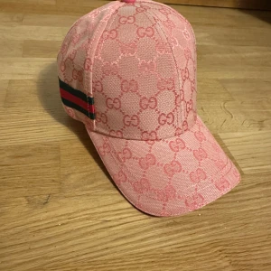 Rosa Gucci keps med GG-mönster - Snygg rosa keps från Gucci med klassiskt GG-monogram över hela kepsen och ikoniska gröna/röda ränder på sidan. Tillverkad i bomull och polyester, justerbar rem bak i ljusrosa läder. Perfekt för dig som vill sticka ut med lyxig streetstyle.