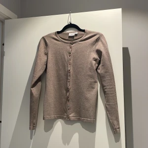 Beige kofta från Saint Tropez - En stilren beige kofta från Saint Tropez i storlek S. Koftan har rund halsringning, långa ärmar och knäppning med matchande knappar framtill. Perfekt att slänga över en t-shirt eller klänning för en chill och snygg look. Använd 2 gånger! Nypris: 400kr
