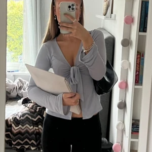 Ljusblå topp med knyt - Ljusblå långärmad topp i trikå från Gina Tricot. Knytdetalj framtill och har V-ringning. Endast använd fåtal gånger, inga defekter. 💞