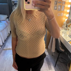 Beige stickad topp från Design by Si - Snygg beige stickad topp från Design by Si med korta ärmar och rund hals. Tunt, genombrutet mönster som ger en luftig känsla. Det står ingen strolek på tröjan men skulle säga att den passar S/M🌼