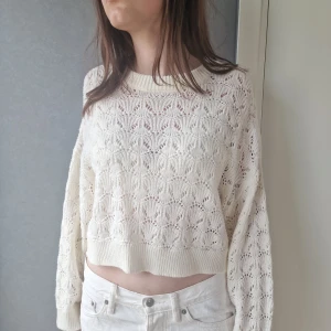 Vit stickad croppad tröja med mönster - Superfin vit stickad tröja med genombrutet mönster och croppad passform. Tröjan har långa ärmar och ribbade muddar vid hals, ärmslut och nederkant. Perfekt för vår och sommar när du vill ha en luftig och snygg look.