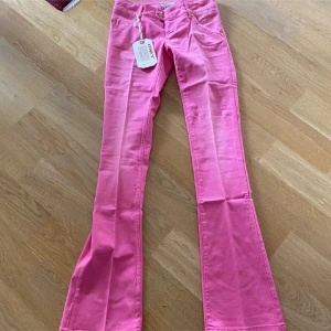 Rosa bootcut jeans från MET - Snygga rosa jeans från MET med bootcut passform och låg midja. Byxorna har klassiska fem fickor, dubbla guldknappar och är tillverkade i ett stretchigt bomullsmaterial.  Mijdemått 36 cm och innerbenslängd 85 cm. 