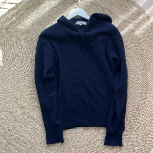 Kashmir hoodie - Mysig mörkblå hoodie från Carmes i mjuk ull. Klassisk modell med huva och dragsnören, samt långa ärmar. Perfekt för kyliga dagar och enkel att matcha med jeans eller joggers. Inga defekter.