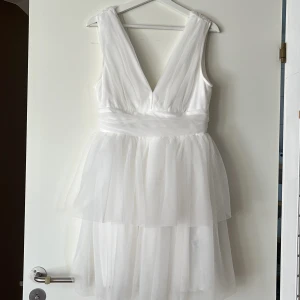 Vit omlottklänning från Gina Tricot - Supersöt vit kortklänning från Gina Tricot med omlottliv och djup v-ringning. Klänningen har lager på lager av tunn tyll, markerad midja och dragkedja i ryggen. Perfekt för dig som vill ha en romantisk och luftig look. Använd 1 gång