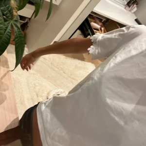 Vit t-shirt med spetsdetalj - Vit t-shirt i bomull med korta ärmar och snygg spetskant längst ner på ärmarna. Enkel och fräsch design med rund halsringning, perfekt för dig som gillar en söt och stilren look.