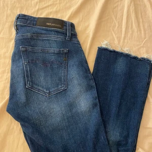 Blå Replay jeans - Snygga blå jeans från Replay med klassisk femficksdesign och råa, fransiga benslut. Jeansen har dragkedja och knapp framtill samt en mörk tvätt som ger en cool vibe.