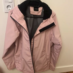 Ljusrosa vindjacka från Everest - Snygg ljusrosa vindjacka från Everest med svart krage och meshfoder. Jackan har dragkedja framtill, praktiska fickor och en sportig look. Perfekt för dig som gillar stilren och funktionell design.