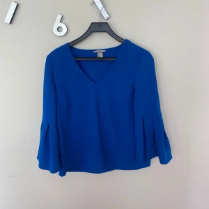 Blå blus med v-ringning H&M - Blå blus från H&M med v-ringad hals och vida, veckade ärmar. 