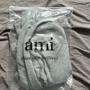 Grå sweatshirt från Ami Alexandre Mattiussi - Snygg grå sweatshirt från Ami Alexandre Mattiussi med ikoniskt hjärta-A broderi på bröstet. Tröjan har rund hals, ribbade muddar och är tillverkad i mjuk bomull. Perfekt för en clean och stilren look.