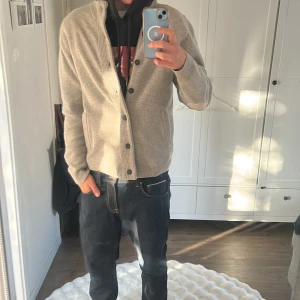 Cardigan ifrån Barbour - Snygg beige kofta med knappar och ribbade muddar. Koftan har hög krage och coola mockadetaljer på armbågarna. Perfekt för lager-på-lager och passar till både jeans och chinos. Två fickor framtill och stilren look. Slutsåld på de flesta ställen just nu😊