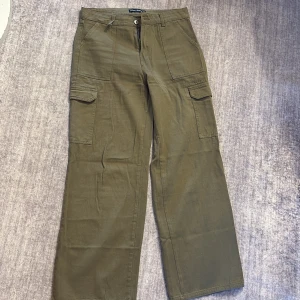 Olivgröna cargopants - Snygga olivgröna cargopants från Meet Sixty med raka ben och stora fickor på sidorna. Byxorna har normal midja och är gjorda i bomull, vilket gör dem både bekväma och slitstarka. Perfekta för en avslappnad streetstyle-look. OBS ENDA SKADAN ÄR DET SOM SYNS PÅ ANDRA BILDEN. 