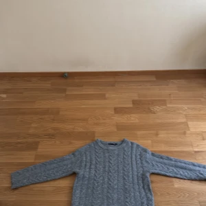 Grå stickad tröja från 157 - Mysig grå stickad tröja från 157 med klassiskt kabelstickat mönster. Tröjan har rund halsringning och långa ärmar, perfekt för lager på lager under kyliga dagar. Enkel att matcha med jeans eller kjol för en avslappnad look.