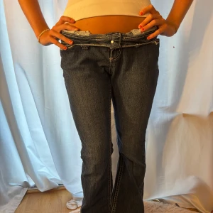 Mörkblå bootcut jeans med broderi - Säljer ett par mörkblå jeans från Love X Ation med bootcut passform och låg midja. Jeansen har snygga kontrastsömmar och detaljerade broderier på bakfickorna. Klassisk femficksmodell i stretchig denim som sitter bra.