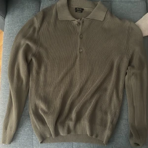 Olivgrön pikétröja från Massimo Dutti - Snygg olivgrön pikétröja från Massimo Dutti i 100% bomull. Tröjan har ribbad struktur, klassisk krage och tre knappar framtill. Perfekt för dig som gillar en stilren och avslappnad look med lång ärm och mjukt material. Nypris 700 säljer för 180