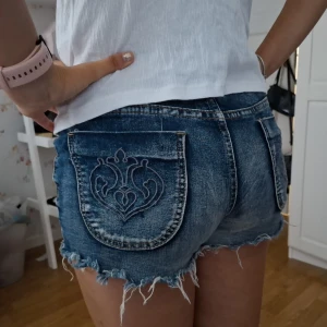 Lågmidjade jeansshorts  - Snygga blå jeansshorts med slitna kanter och broderade bakfickor. Knappt använda, säljer då de inte passar. Storlek 25