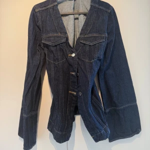 Mörkblå jeansjacka med vida ärmar - Snygg mörkblå jeansjacka med markerade sömmar och vida ärmar. Jackan har två bröstfickor med lock och knappar framtill. Figurnära passform.
