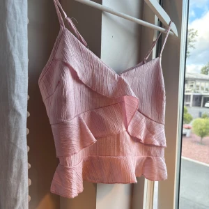 Ljusrosa volangig linnetopp - Supersöt ljusrosa linnetopp med tunna axelband och flera lager volanger. Toppen ger en söt och trendig look, perfekt för varma dagar. 💕
