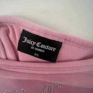 Rosa velourklänning Juicy Couture XS - Superfin rosa kortklänning från Juicy Couture i mjuk velour med smala axelband. Framsidan har glittrande Juicy Couture-logga i strass. Perfekt för dig som älskar 2000-talsvibbar och vill sticka ut med en ikonisk look.