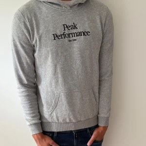 Grå hoodie från Peak Performance - Otroligt snygg grå hoodie från Peak Performance med svart broderad logga på bröstet. Storlek 170/S cirka 185cm lång kille på bilden. Bra pris 