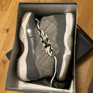 Air Jordan 11 Retro Cool Grey - Säljer ett par Air Jordan 11 Retro i färgen Cool Grey. Skorna har en snygg mix av grå mocka och blankt syntetmaterial, vit mellansula och genomskinlig yttersula. Klassisk Jumpman-logga på hälen och vita snören. Perfekt för dig som vill sticka ut med en ikonisk sneaker.