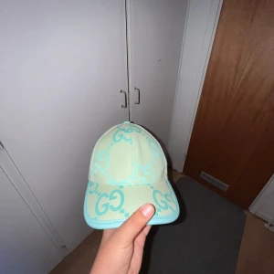 Mintgrön  keps med GG-logga - Säljer en snygg mintgrön med stora GG-loggor i turkos över hela kepsen. Kepsen har böjd skärm och justerbar rem bak. Tillverkad i bomullsmix med detaljer i syntet. Perfekt för dig som vill sticka ut med en exklusiv accessoar.