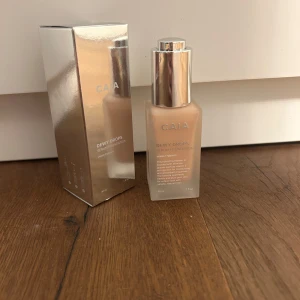 CAIA Dewy Drops Serum Foundation 20C - CAIA Dewy Drops Serum Foundation i nyansen 20C. Den har aldrig använts, så den är helt full. Ger en naturligt daggig finish och innehåller vitamin E och glycerin för extra återfuktning. 30 ml. Perfekt för dig som vill ha en fräsch och glowig bas.