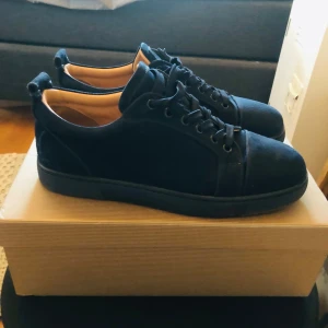 Svarta sneakers från Christian Louboutin - Snygga svarta sneakers från Christian Louboutin i mocka med klassisk rund tå och svarta snören. Skorna har en stilren design med diskreta detaljer och svart sula. Perfekta för dig som gillar exklusiva och minimalistiska sneakers.