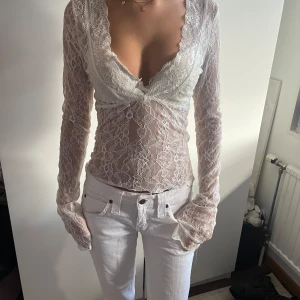 Vit spetsblus med v-ringning - Superfin vit blus i spets med djup v-ringning och långa ärmar från Nelly. Blusen har blommigt spetsmönster och är transparent, perfekt för att skapa en romantisk och trendig look. Snygg att styla med jeans eller kjol för en cool outfit. Endast använd fåtal gånger!!