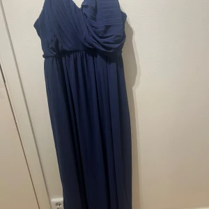 Marinblå långklänning TFNC London - Säljer en marinblå långklänning från TFNC London. Klänningen har ett snyggt draperat liv med omlott och en axelbandslös design. Tyget är lätt och faller fint, perfekt för bal eller fest. Klassisk och elegant look som sticker ut.