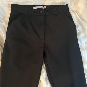 Svarta kostymbyxor från 157 - Klassiska svarta kostymbyxor från 157 med raka ben och diskreta sidfickor. Byxorna har hällor för bälte och stängs med knapp och dragkedja. Perfekta för en clean och stilren look.