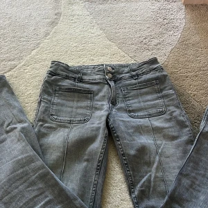 Grå jeansbyxor  - Snygga grå jeansbyxor från Gina Young med raka ben och stora fyrkantiga fickor både fram och bak. Byxorna har dubbla knappar i midjan och dragkedja. Jeansen är i skönt mjukt jeans tyg 