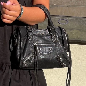 Mini Svart Balenciaga väska - Cool svart handväska från Balenciaga i skinn med silverfärgade metalldetaljer, dragkedjor och nitar. Klassisk city-modell med dubbla handtag och dekorativa remmar 🩷 