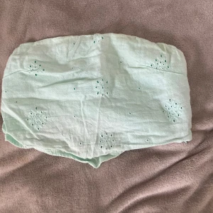 Mintgrön bandeau tubtopp från Bershka - Söt mintgrön bandeau tubtopp från Bershka med broderade blommönster och små hål som ger en luftig känsla. Toppen är ärmlös och har resår upptill och nedtill för att sitta på plats. Perfekt för varma dagar och sommarvibbar.