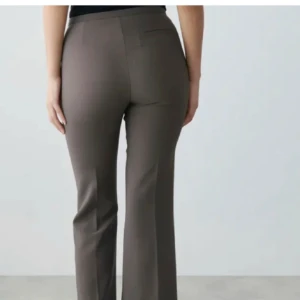 Gråa bootcut kostymbyxor - Snygga gråa kostymbyxor med bootcut-snitt och hög midja. Byxorna har klassisk passform och raka ben som släpper ut nertill. Perfekta för en clean och stilren look. Materialet är slätt och ger en dressad känsla.