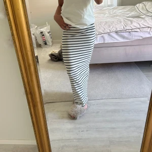 Randig långkjol med slits - Säljer en snygg långkjol i vitt med svarta horisontella ränder. Kjolen har en tight passform och en slits på sidan som ger en chill vibe. Perfekt till sneakers eller sandaler. Materialet känns mjukt och stretchigt, troligen bomull eller polyester.