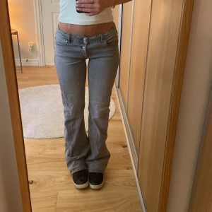 Grå bootcut jeans från Gina Tricot - Säljer ett par grå jeans från Gina Tricot young med låg midja och bootcut-ben. Jeansen har tre silverfärgade knappar framtill, klassiska fickor och är tillverkade i mjukt denimtyg.💗