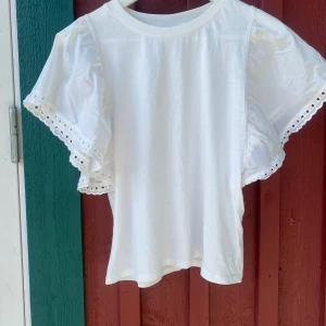 Vit blus med volangärm från Kappahl - Supersöt vit blus från Kappahl med breda volangärmar och broderade spetsdetaljer längs ärmsluten. 