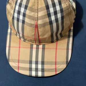 Beige rutig keps från Burberry - Snygg keps i klassiskt beige rutigt mönster från Burberry. Kepsen har böjd skärm och justerbar passform. Perfekt accessoar för en trendig look.