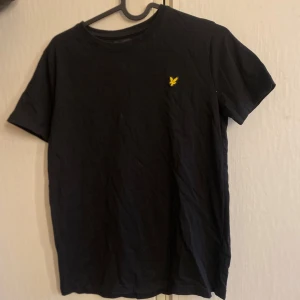 Svart t-shirt från Lyle & Scott Junior - Svart t-shirt från Lyle & Scott Junior med klassisk rund hals och liten gul logga på bröstet. Enkel och stilren modell som passar perfekt till vardags. Tillverkad i mjuk bomull för skön komfort. Jag som är 161 har kunnat använda tröjan så den passar även dig som har S