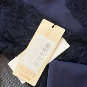 Marinblå långklänning med spetsärmar från Club L - Elegant marinblå långklänning från Club L med långa spetsärmar och vacker volangdetalj framtill i midjan. Klänningen har figurnära passform upptill och är tillverkad i ett mjukt, följsamt material. Perfekt för speciella tillfällen.