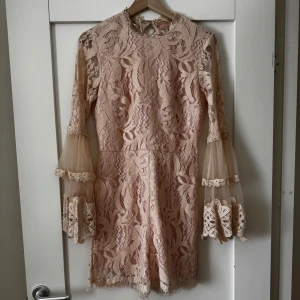 Champagnefärgad spetsklänning med volangärmar - Säljer en superfin champagnefärgad kortklänning med shorts och med spets och transparenta volangärmar. Klänningen har rund halsringning och vackra spetsdetaljer över hela plagget. Perfekt för dig som vill sticka ut med en romantisk look.