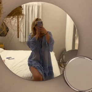 Ljusblå volangklänning med detaljer - Säljer en ljusblå klänning med v-ringning och fina broderade detaljer längs halsen. Lite utomlands vibe! Köpt på en marknad i Grekland. Funkar perfekt som både klänning och beach cover up! Lite genomskinlig men inte så farligt. Endast använd 2 ggr. Köpte för 500kr därav priset. Pris kan diskuteras. Hör gärna av dig!🥰